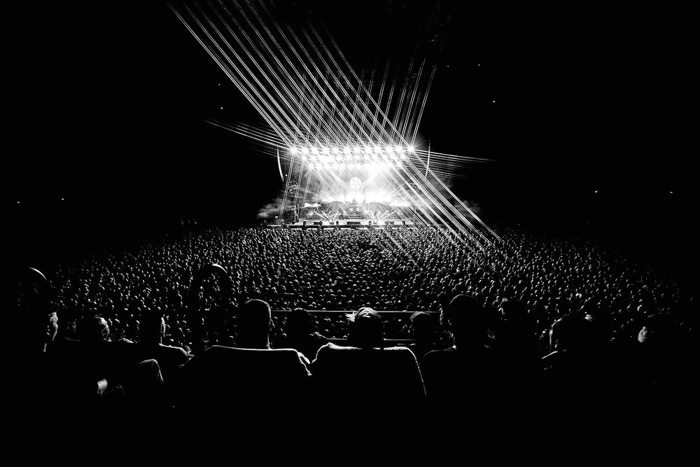 Black and white photo of a large crowd watching a brightly lit stage at a concert.