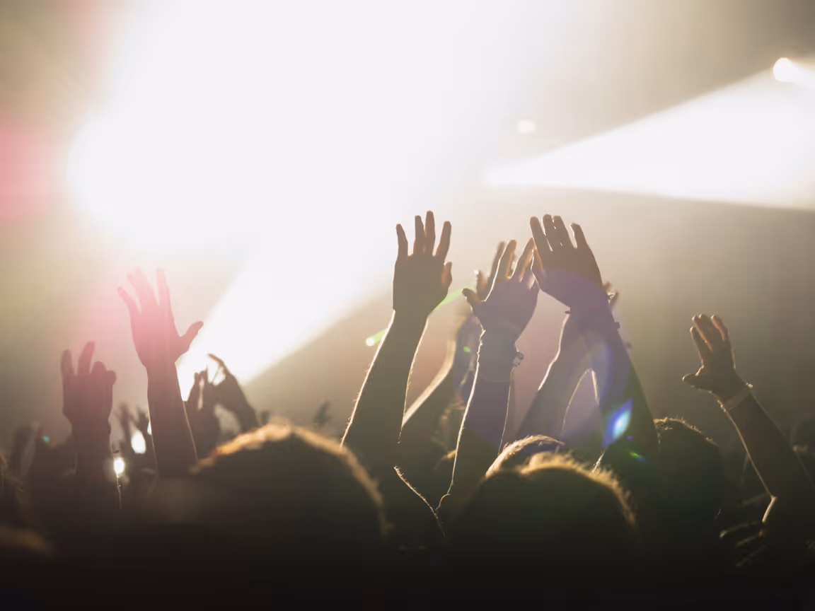Crowd with raised hands enjoying a live music concert under bright stage lights.