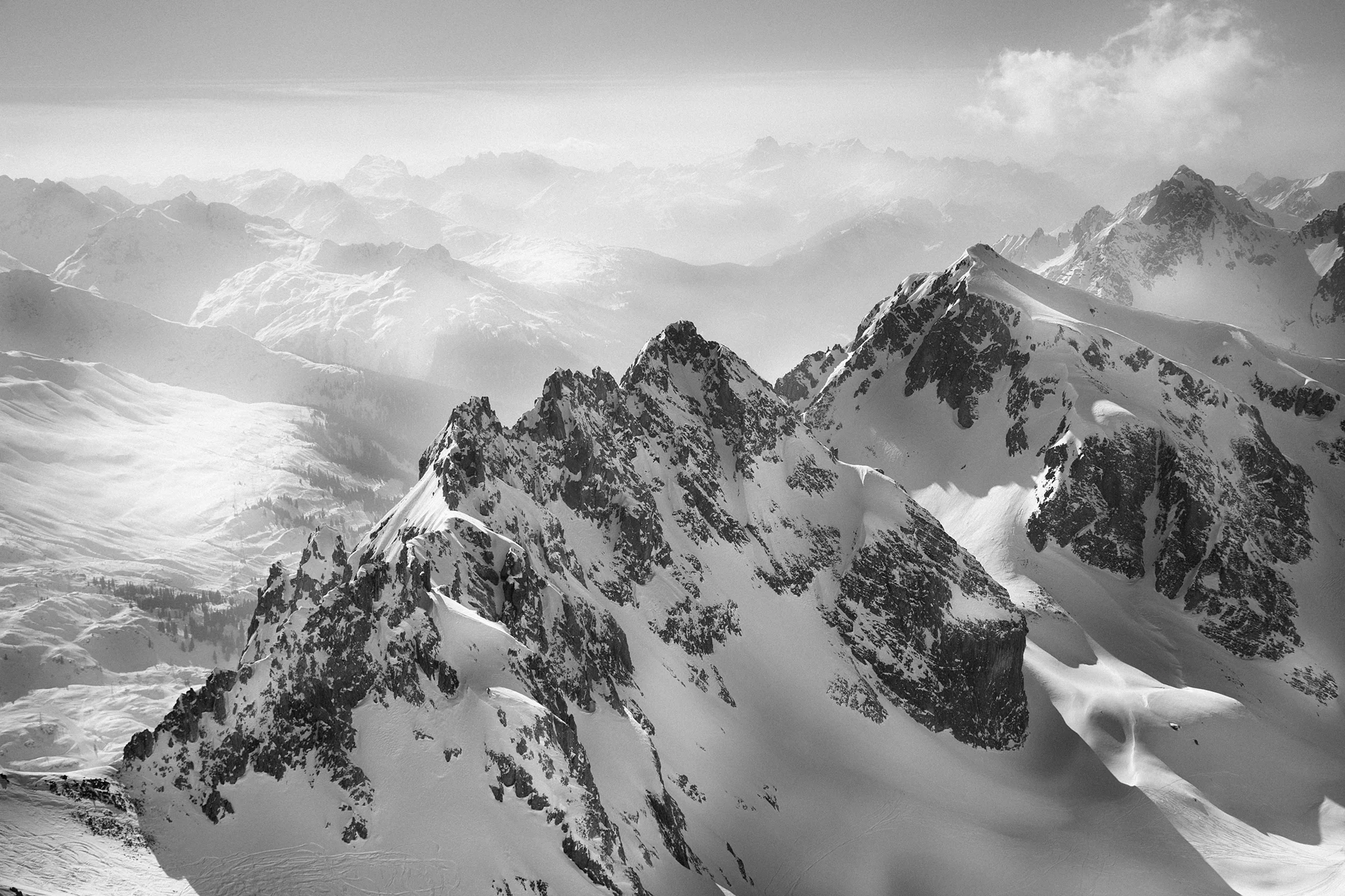 Snow-covered rugged mountain peaks under a cloudy sky with distant mountain ranges fading into the mist.