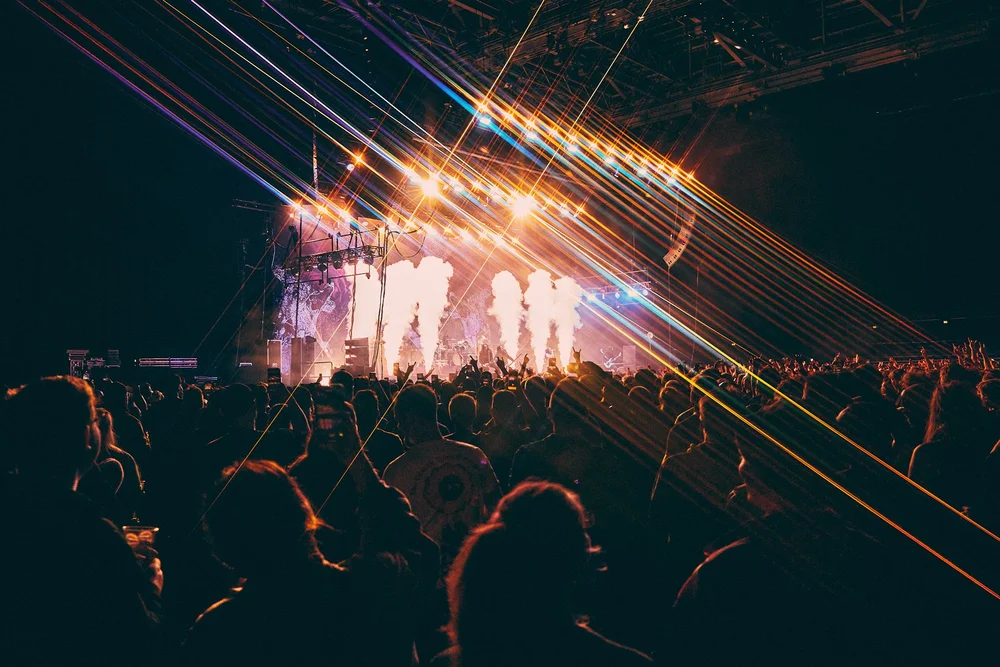 Crowd watching a concert with bright stage lights and smoke effects at night.